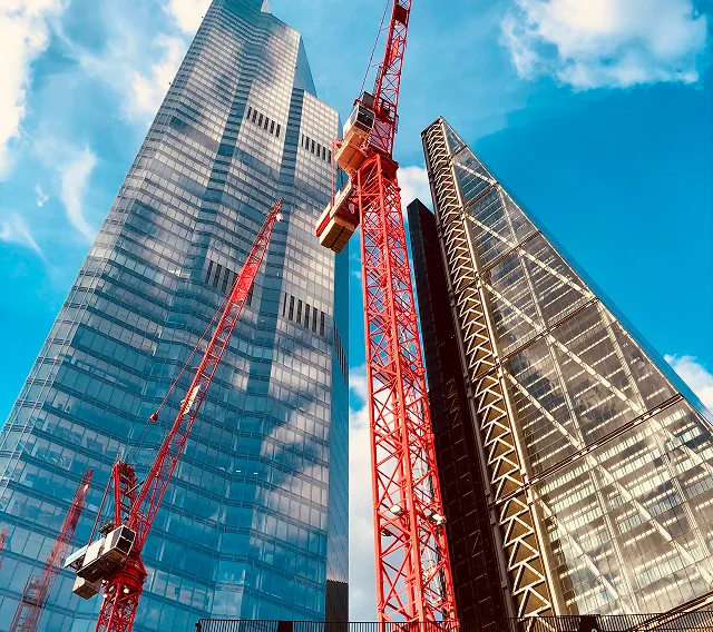 Tower cranes rising alongside modern high-rise towers on an active construction site, viewed from below